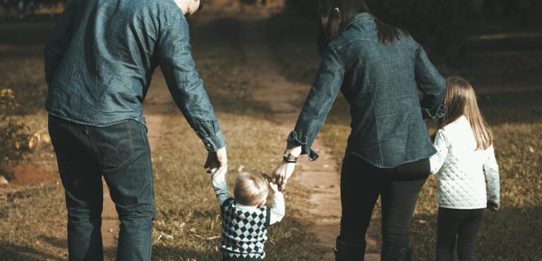 A family of four walks hand in hand on a path, enjoying a sunny day outdoors.