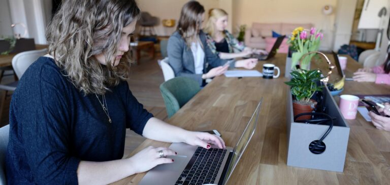 Group of women working in a modern coworking space with laptops and coffee.