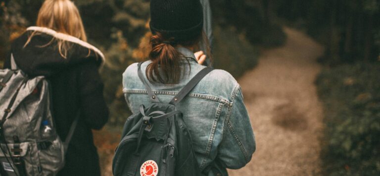 Two friends explore a forest trail together with backpacks, enjoying nature.