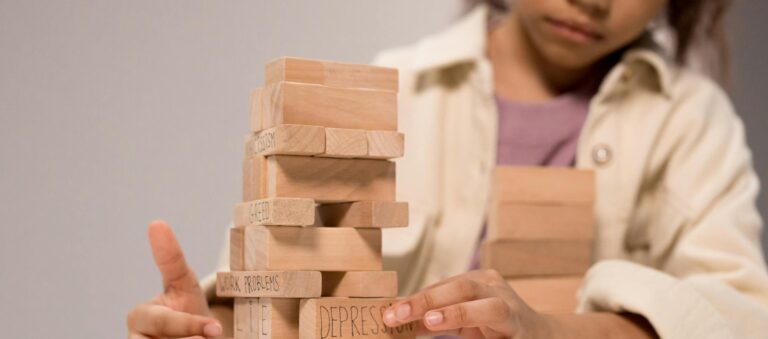 A child thoughtfully stacks wooden blocks with words like 'depression' and 'kindness.'