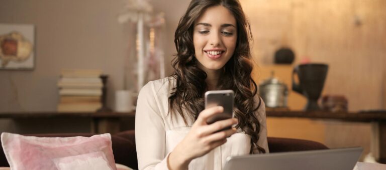 A woman enjoying leisure time using her smartphone and laptop in a cozy living room.