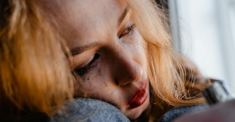 Close-up of a woman with red hair in a thoughtful and emotional moment indoors.