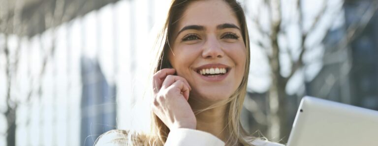 Confident businesswoman using her tablet and phone, smiling outdoors in sunlight.