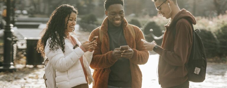 Three diverse young adults enjoying social media together in a sunny park.