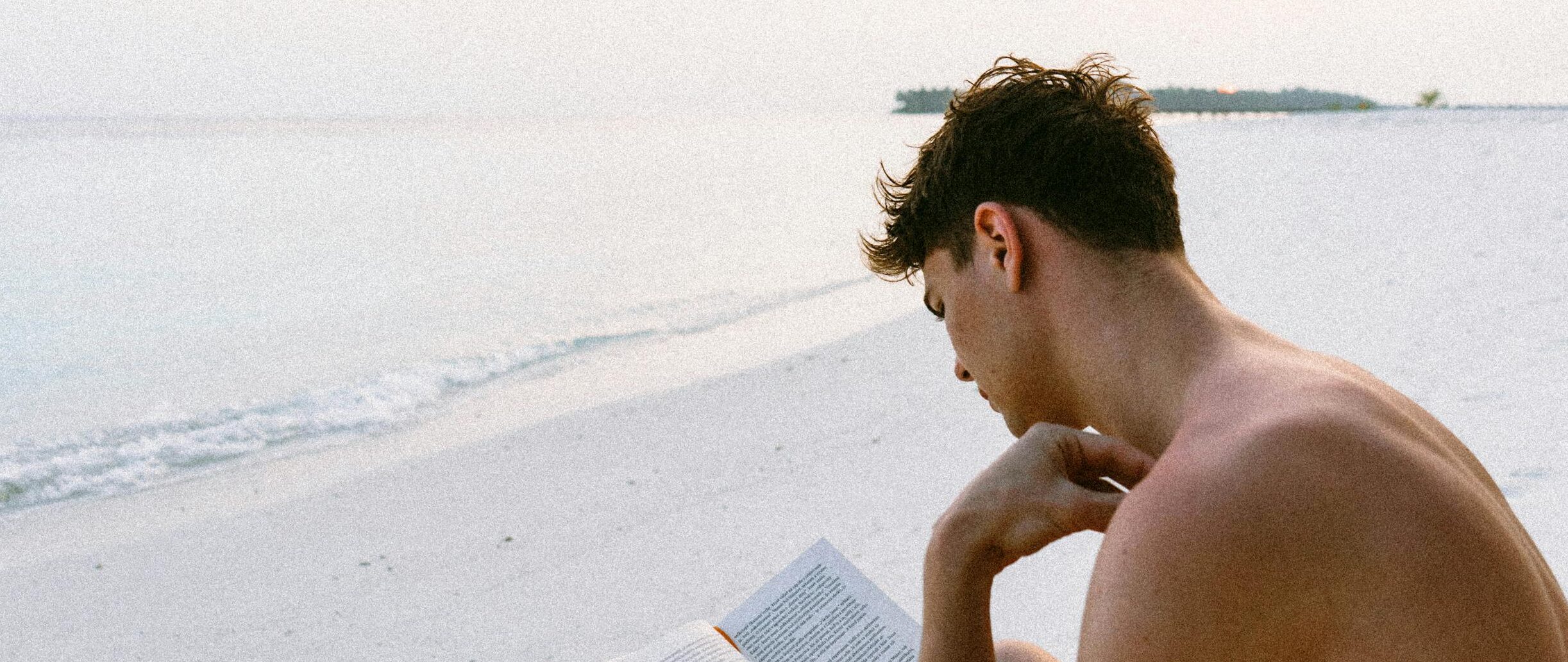 A man enjoys reading a book on a serene Maldives beach, capturing the essence of relaxation.