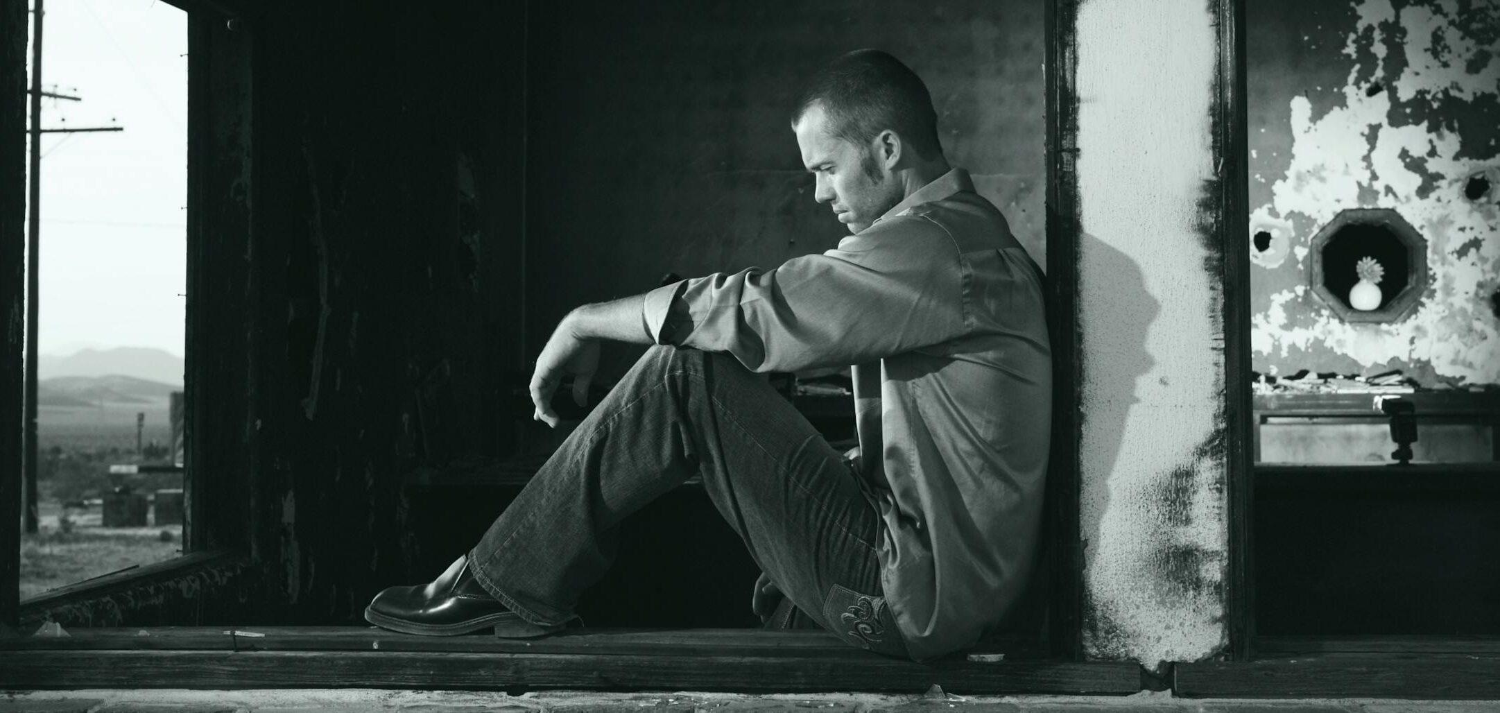 A young man sits pensively in a derelict building, embodying solitude and contemplation.
