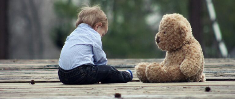 Adorable toddler sitting with a teddy bear on a wooden bridge, enjoying a peaceful moment outdoors.