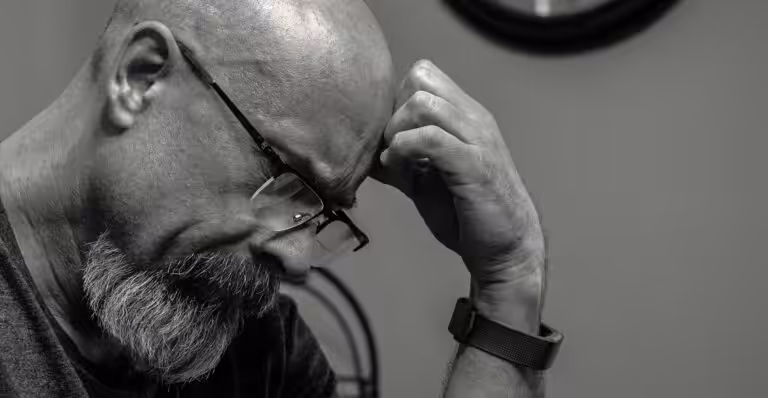Black and white portrait of a thoughtful bald man indoors, capturing a moment of reflection with a wall clock in the background.