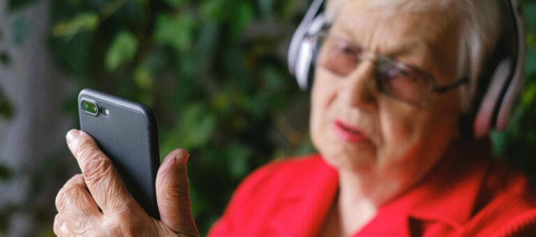 Senior woman in red using smartphone with headphones outdoors.