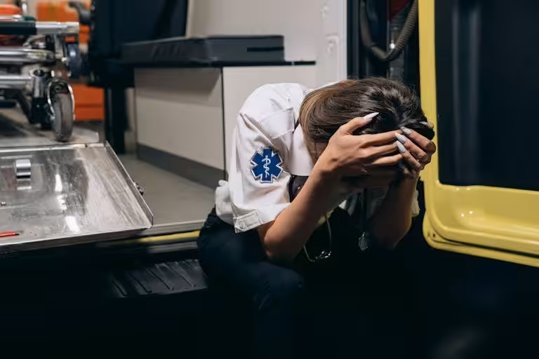 EMT in distress sitting inside an ambulance, head in hands signifying stress and exhaustion.